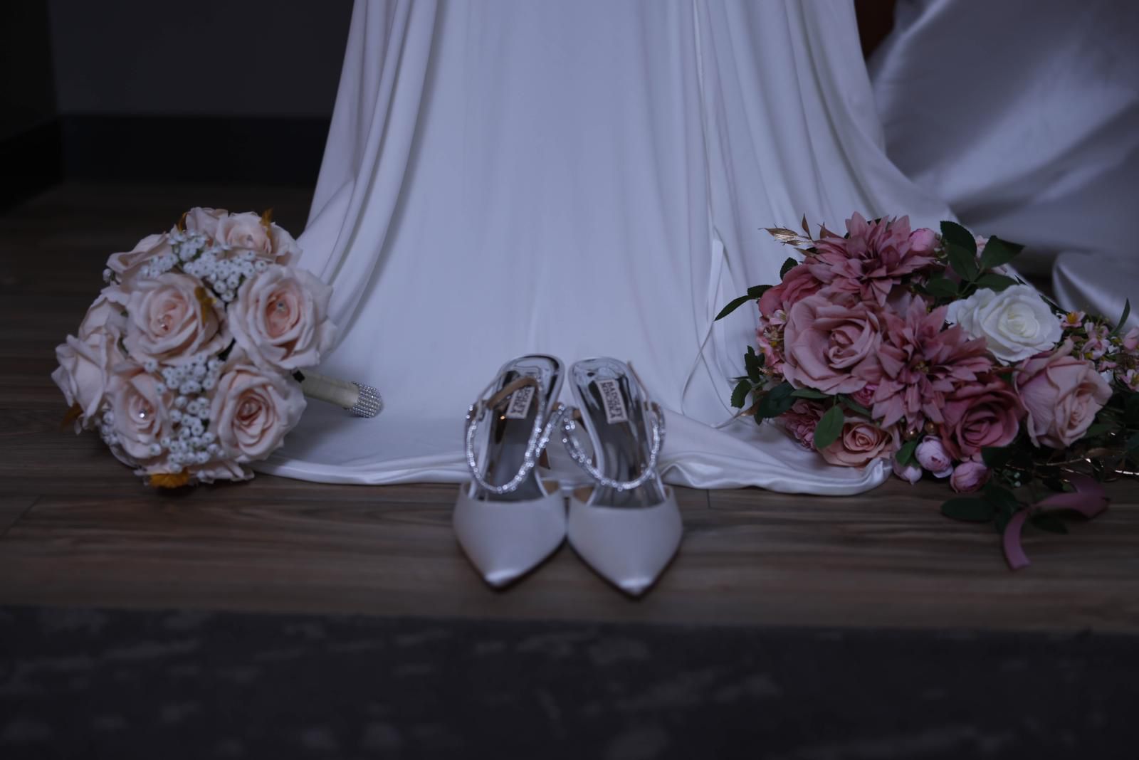 Bridal bouquets and shoes arranged beside the wedding gown